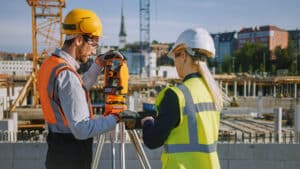 Man speaking to woman about IT outdoors at construction site, both wearing construction gear